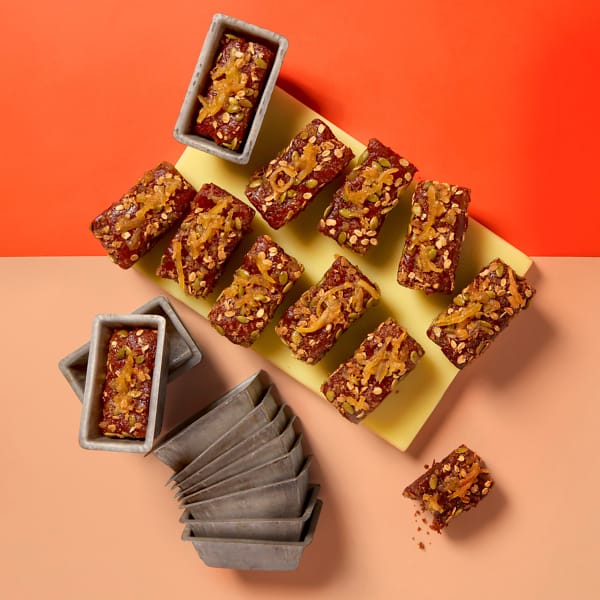 A full tray of vegan Sticky Ginger and Lemon Mini Loaf cakes by Cake Club on a yellow board with an orange and peach contrasting background.