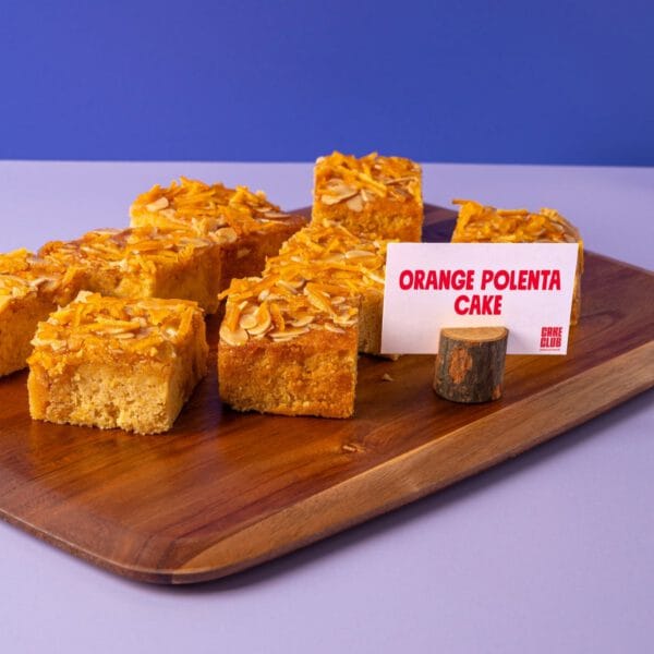 Orange Almond and Polenta Traycake displayed on a wooden board with a product sign.