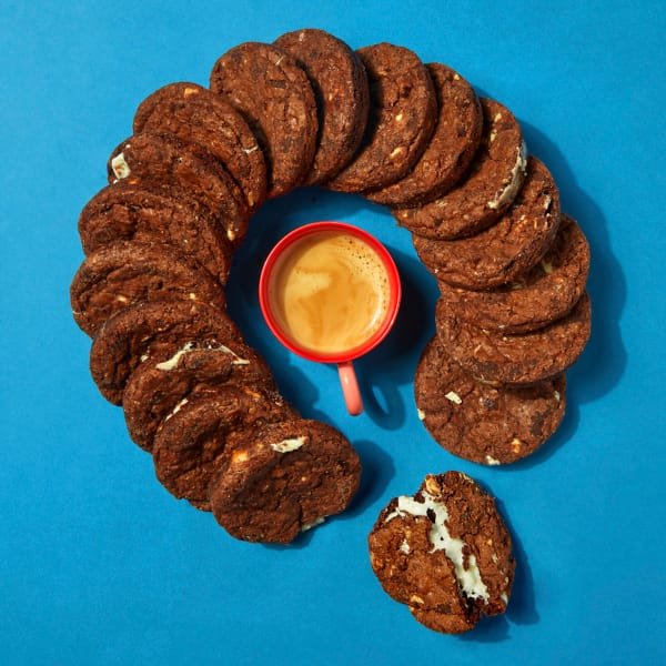 A whole case of Chocolate Smores Cookies stacked like dominoes around a cup of coffee with a blue background.