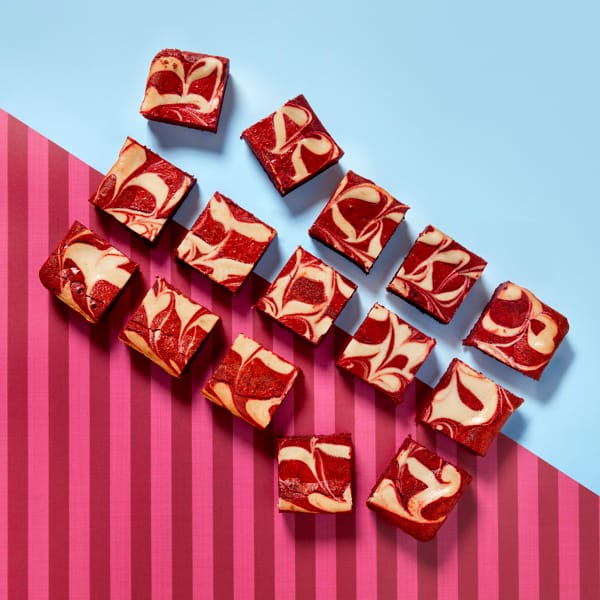 A full tray of delicious Cake Club Red Velvet Brownies lined diagonally on a claret and light blue contrasting background.